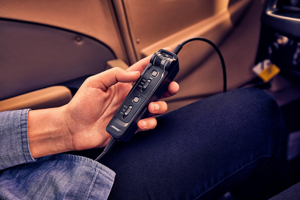 Modulo de controle do Bose A30 na mao do piloto, com volume, seletor de cancelamento em tres niveis, botao Bluetooth e chave mute mix off